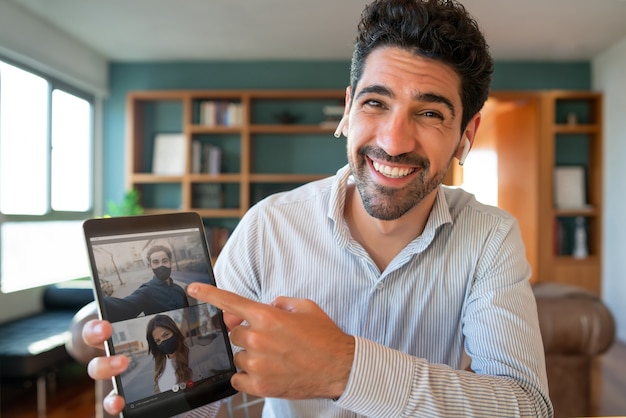 Uomo che utilizza la tavoletta digitale durante una videochiamata con i suoi amici mentre si è a casa.