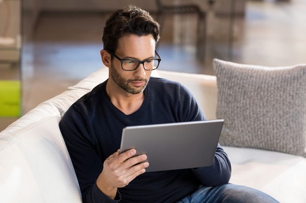 Uomo che utilizza la tavoletta digitale sul divano di casa.