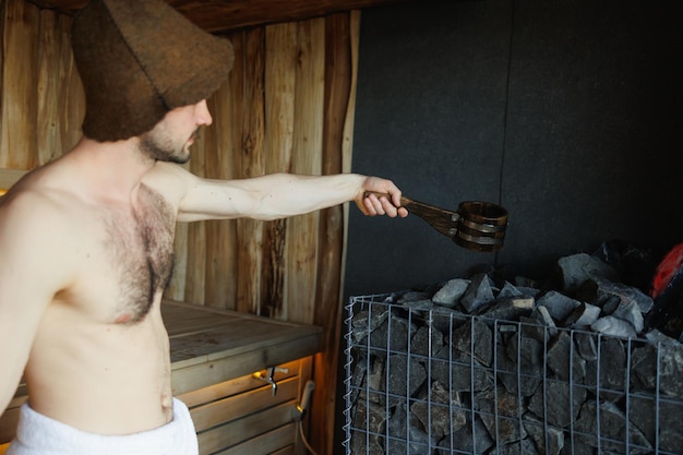 Uomo che versa acqua nella pietra nella stanza della sauna