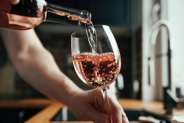 Uomo che versa vino rosato ai bicchieri dalla bottiglia in cucina bicchieri da vino trasparenti e riempimento sommelier