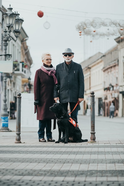 Uomo cieco maturo con un lungo bastone bianco e sua moglie che camminano con il loro cane guida.