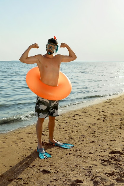 Uomo con anello gonfiabile pinne e occhiali sulla spiaggia del mare