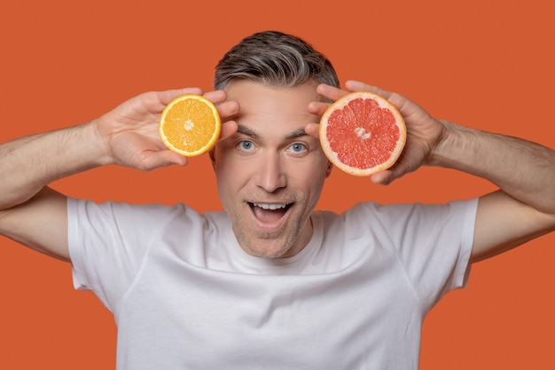Uomo con arancia e pompelmo vicino al viso