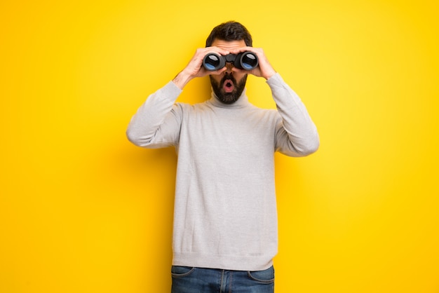 Uomo con barba e collo alto e guardando in lontananza con il binocolo