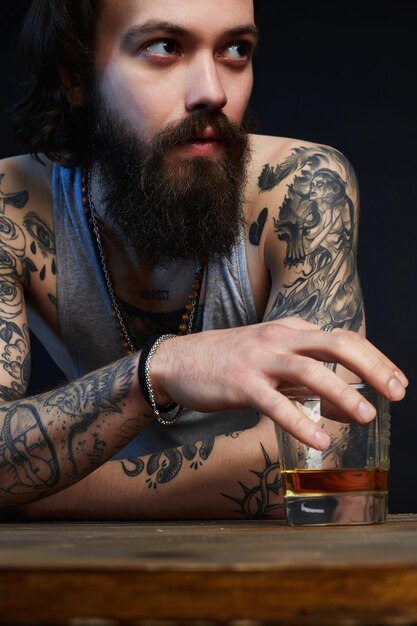 Uomo con barba e tatuaggio con bicchiere di whisky