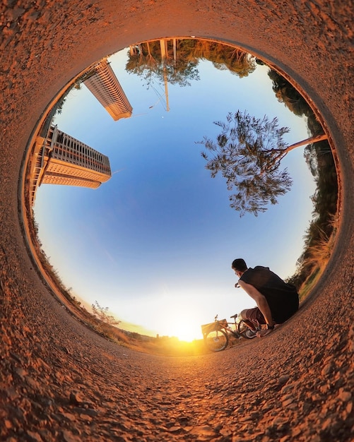 Uomo con bicicletta sul piccolo pianeta con alberi morbido cielo blu e tramonto Mini pianeta di un parco e tramonto