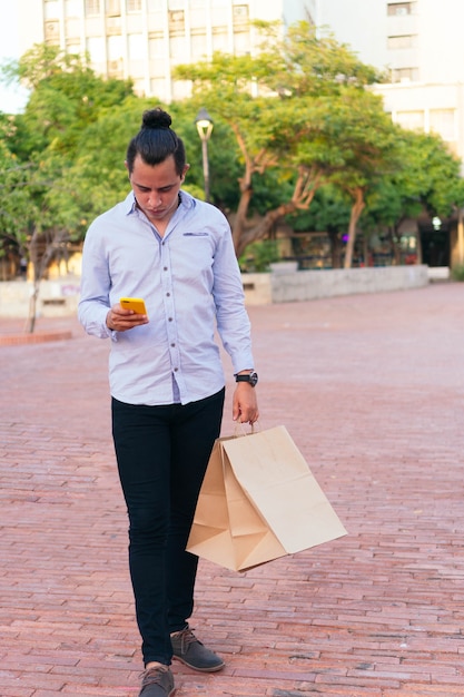 Uomo con borsa ecologica che controlla il cellulare cammina per strada