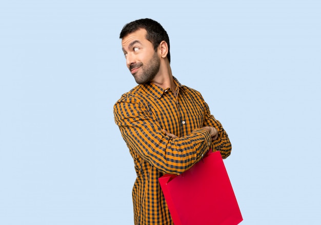 Uomo con borse della spesa guardando oltre la spalla con un sorriso su sfondo blu isolato