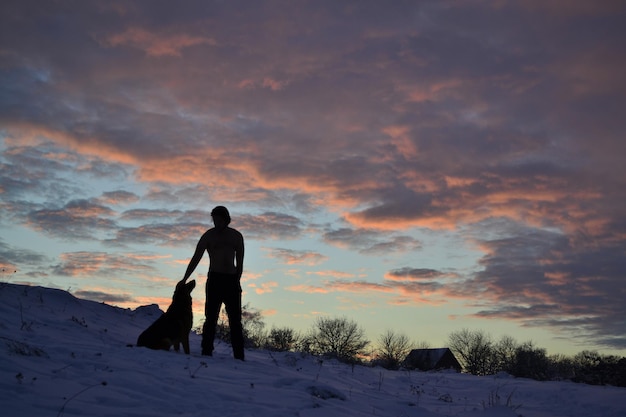 uomo con cane in inverno al tramonto