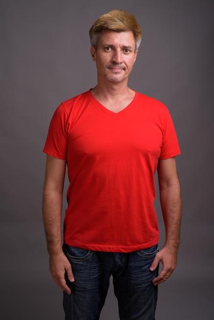 Uomo con capelli biondi che indossa la camicia rossa contro il muro grigio