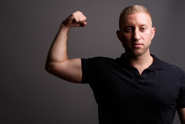 Uomo con capelli biondi che indossa la polo nera sulla parete grigia