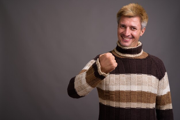 Uomo con capelli biondi che indossa maglione a collo alto isolato contro il muro grigio