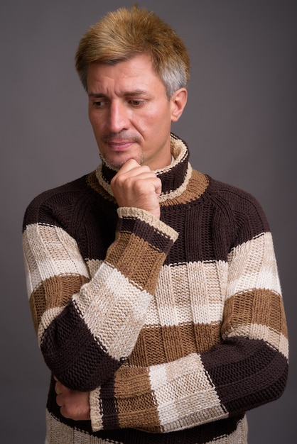 Uomo con capelli biondi che indossa maglione a collo alto isolato contro il muro grigio