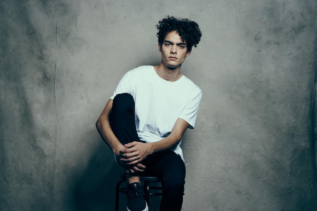 Uomo con capelli ricci che si siede su una sedia studio di moda