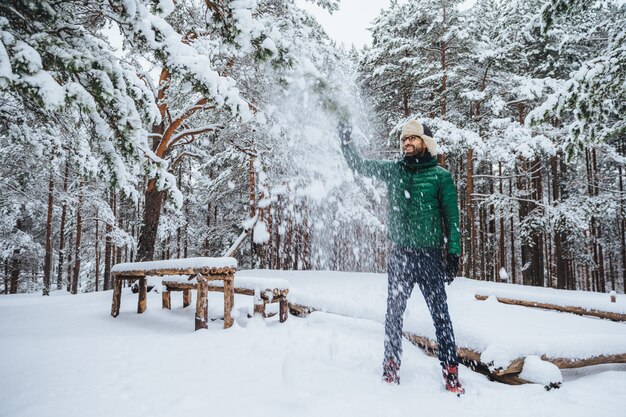 uomo con cappello di pelliccia con paraorecchie che giocano con la neve