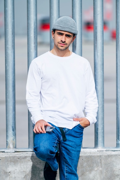 Uomo con cappello, jeans e maglietta bianca in posa sulla strada