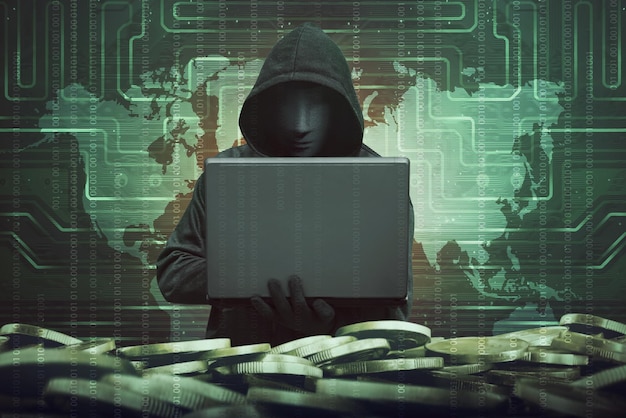 Uomo con cappuccio con maschera anonima che usa un portatile per hackerare la sicurezza del sistema bancario contro il codice binario in background