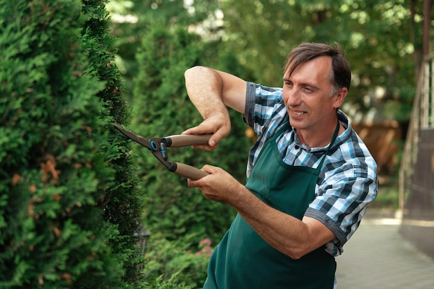 Uomo con cesoie da giardino che tagliano cespugli e alberi in giardino