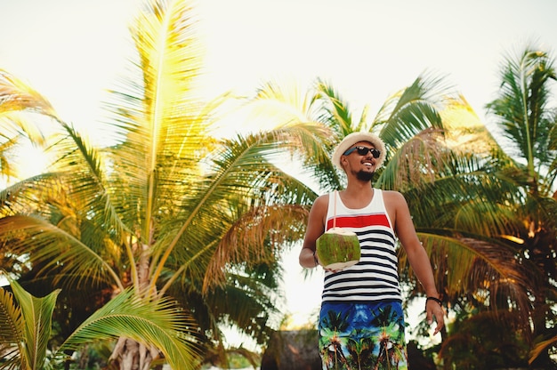 Uomo con cocco sulla spiaggia tropicale nella soleggiata giornata estiva durante le vacanze