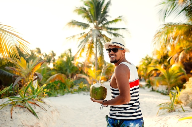 Uomo con cocco sulla spiaggia tropicale nella soleggiata giornata estiva durante le vacanze