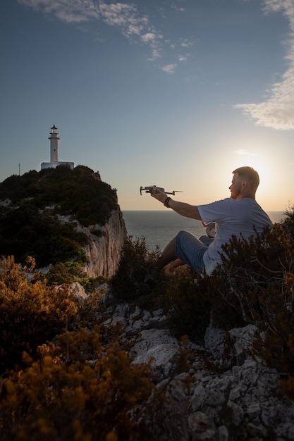 Uomo con drone presso la scogliera vicino al mare tramonto sopra il faro Lefkada Grecia