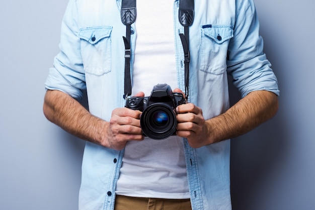 Uomo con fotocamera digitale. Immagine ritagliata di un uomo con una fotocamera digitale in piedi su uno sfondo grigio