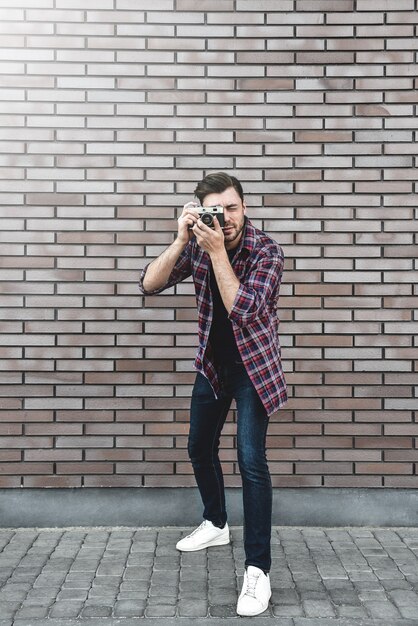 Uomo con fotocamera retrò Fashion Travel Lifestyle all'aperto mentre in piedi contro la superficie del muro di mattoni