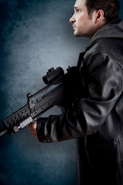 Uomo con giacca di pelle lunga e fucile d'assalto