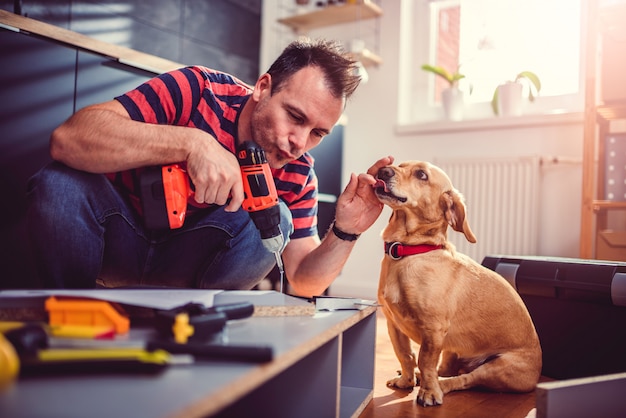 Uomo con gli armadi da cucina della costruzione del cane e per mezzo di un trapano senza cordone