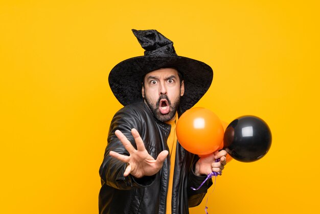 Uomo con il cappello della strega che tiene le mongolfiere nere e arancio per la festa di Halloween che allunga nervosamente le mani alla parte anteriore