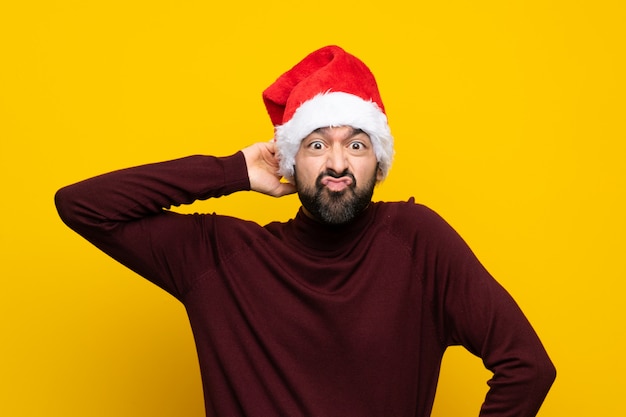 Uomo con il cappello di natale sopra la parete gialla isolata che ha dubbi