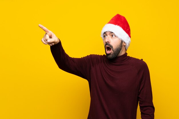 Uomo con il cappello di natale sopra la parete gialla isolata che indica via