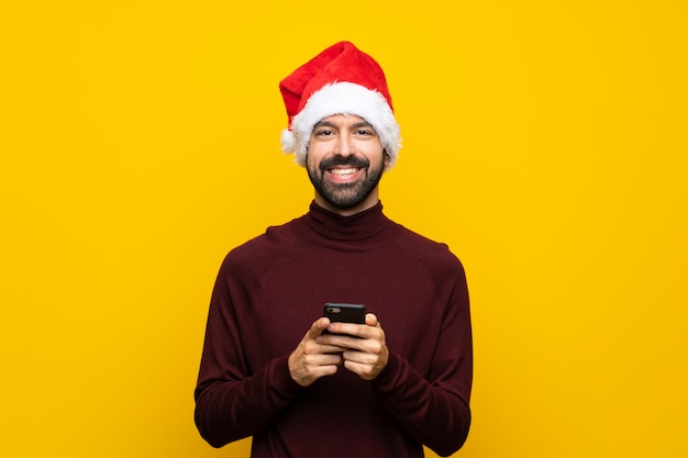 Uomo con il cappello di natale sopra la parete gialla isolata che invia un messaggio con il cellulare