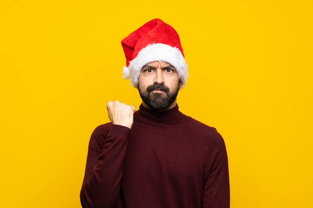 Uomo con il cappello di natale sopra la parete gialla isolata con il gesto arrabbiato