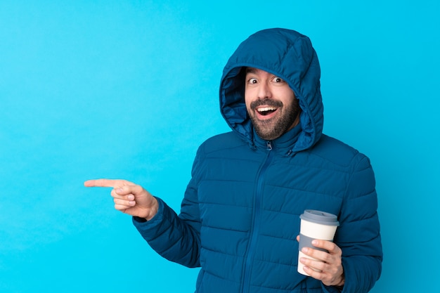 Uomo con il cappotto di inverno sopra la parete blu isolata