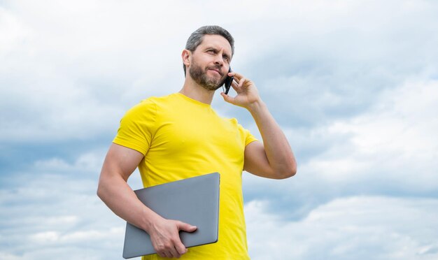 Uomo con il computer che parla sullo smartphone sullo sfondo del cielo