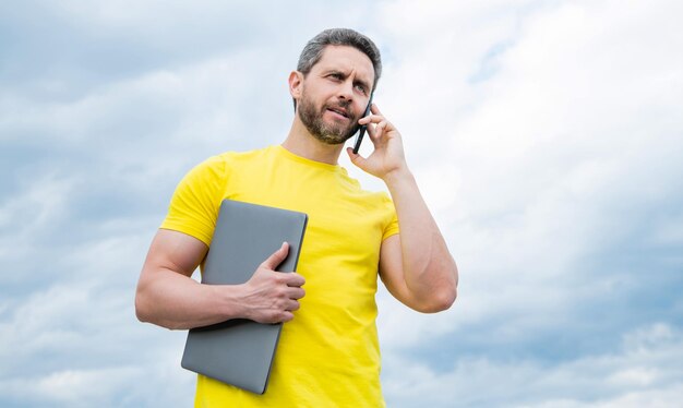 Uomo con il computer portatile che parla sullo smartphone sulla negoziazione del fondo del cielo