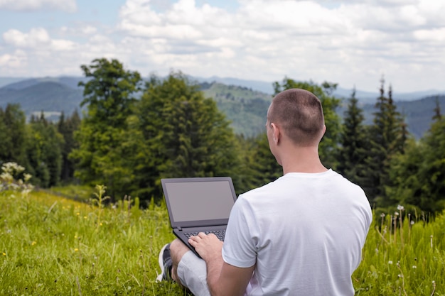 Uomo con il computer portatile che si siede sull'erba verde