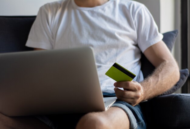 Uomo con il computer portatile e la carta di credito a casa.