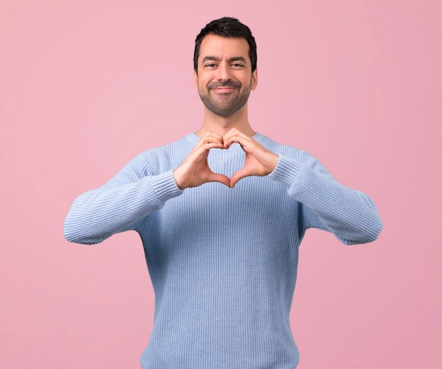 Uomo con il maglione blu che fa il simbolo del cuore a mano