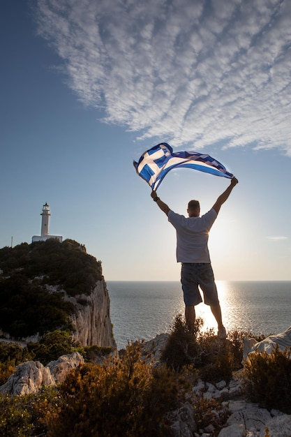 Uomo con la bandiera della grecia che guarda il tramonto sopra il mare