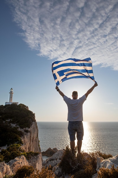 Uomo con la bandiera della grecia che guarda il tramonto sopra il mare