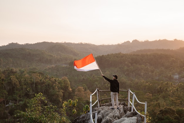 Uomo con la bandiera indonesiana dell'Indonesia in cima alla montagna