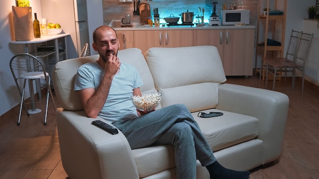 Uomo con la barba che guarda un programma televisivo usando il telecomando per cambiare canale in televisione