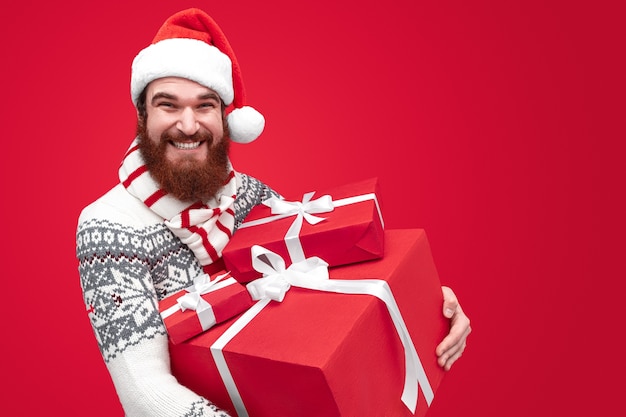 uomo con la barba che indossa il cappello della Santa e che tiene grande mucchio di regali avvolti