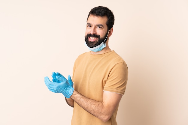 Uomo con la barba che protegge dal coronavirus con una maschera e guanti sopra l'applauso isolato della parete