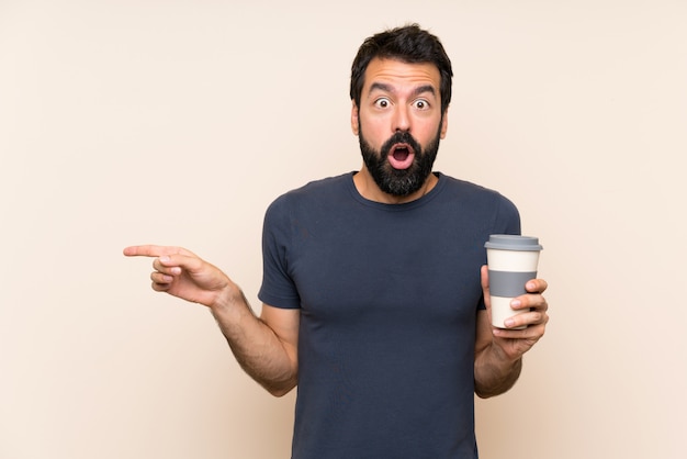 Uomo con la barba che tiene un caffè sorpreso e che indica il lato