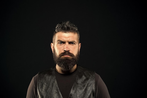 Uomo con la barba in abiti di pelle nera Uomo fiducioso e brutale stile sfondo nero Concetto di barbiere Crescere i baffi Viso rigoroso e maturo Peli sul viso Viso maschile Viso bello Modello di moda