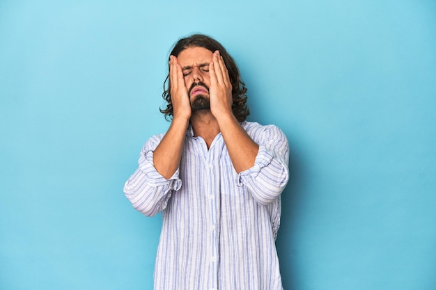 Uomo con la barba in camicia a righe blu che piange infelice per qualcosa concetto di agonia e confusione