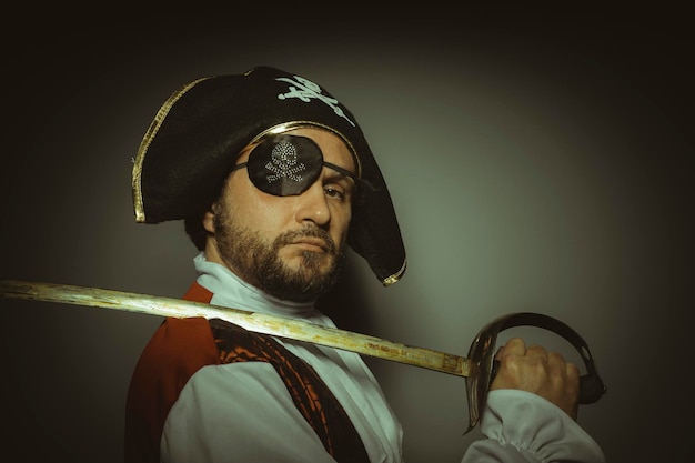 Uomo con la barba vestito da pirata, con benda sull'occhio e spada d'acciaio